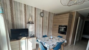 A compact kitchen with a built-in oven, a dining area with a table and chairs, and a TV on a cabinet.