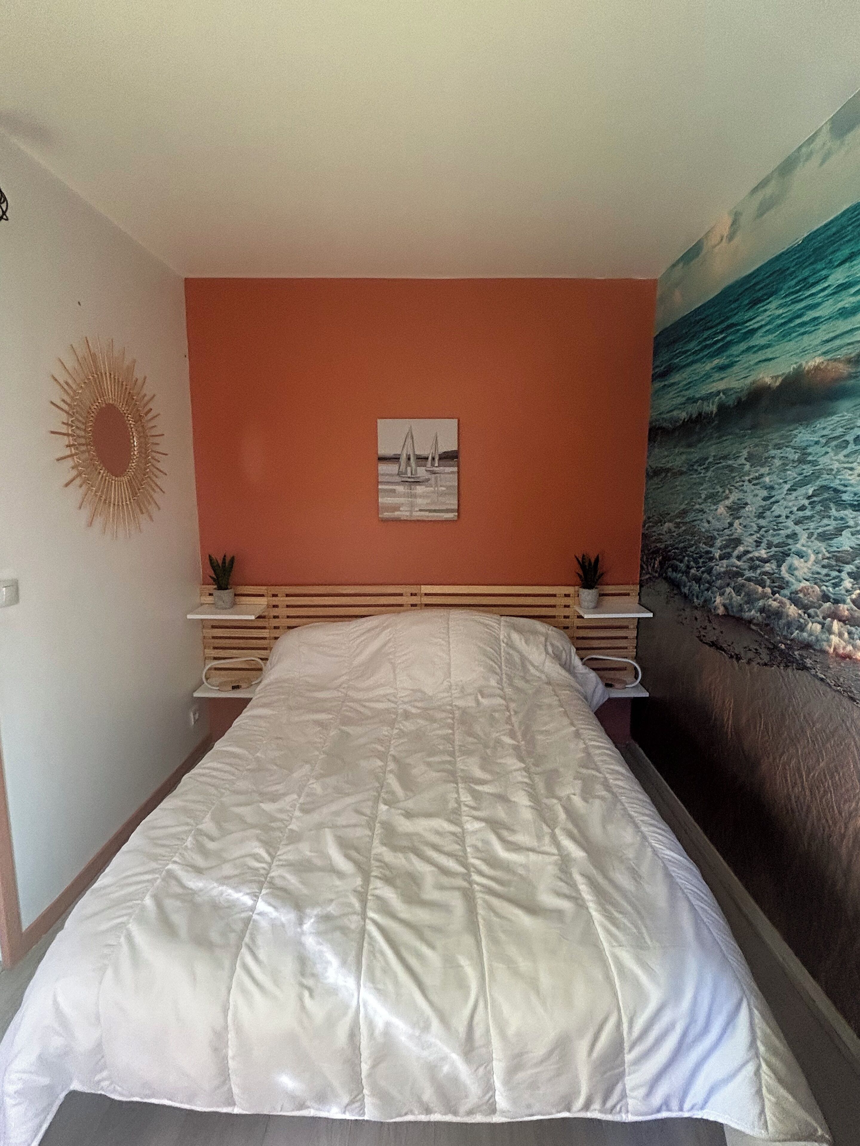 A bedroom with a bed, a wall-mounted picture, a sun decoration, and a beach mural.