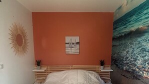 A bedroom with a bed, a wall-mounted picture, a sun decoration, and a beach mural.