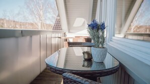 A balcony with wicker furniture, a glass table, and a potted plant.