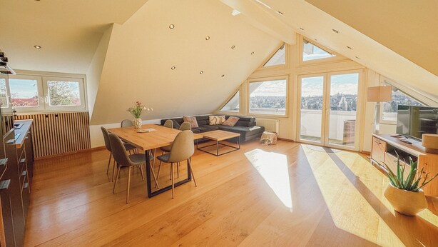 A spacious loft with a dining area, sofa, and a large window offering a city view.