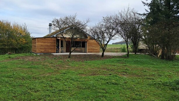Une cabane en bois dotée d’un porche, entourée d’une zone herbeuse et d’arbres.