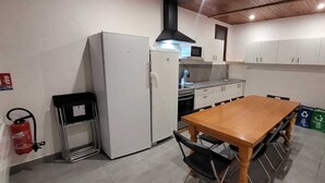 Une cuisine compacte avec un réfrigérateur blanc, une cuisinière et un four à micro-ondes. On y trouve une table à manger en bois avec des chaises. Un extincteur est fixé au mur.