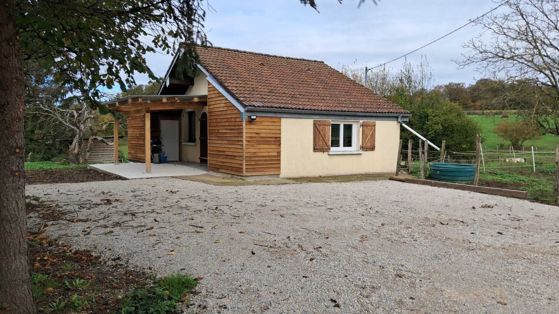 Ein eingeschossiges Haus mit geneigtem Dach, Holzfassade und Auffahrt mit Kies.