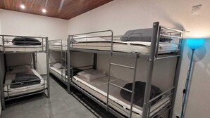 Une chambre de dortoir avec des lits superposés, un plafond en bois et une lampe fixée au mur.