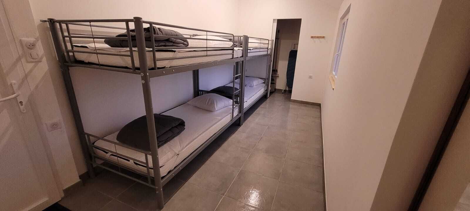 Dormitorio con literas, una puerta, una ventana y suelo de baldosas.