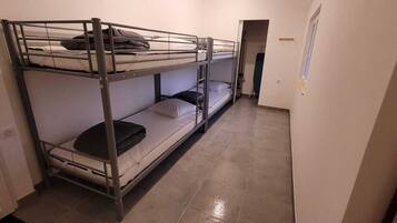 Dormitorio con literas, una puerta, una ventana y suelo de baldosas.