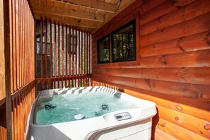 A hot tub in a wooden cabin with a window and a wooden fence.