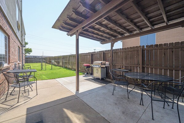 An outdoor patio with a covered seating area, a grill, and a table with chairs. - Affordable Suites of America Tulsa (Tulsa)