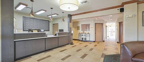 A hotel lobby with a reception desk, a patterned wall, a ceiling fan, and a brown leather couch.