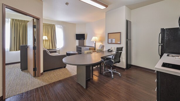 Ein Hotelzimmer mit Esstisch, Stühlen, einem Flachbildfernseher, einem Kühlschrank und einer kleinen Küchenzeile.