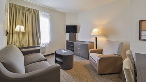 Ein Hotelzimmer mit Sofa, Sesseln, einem kleinen Tisch, einem Fernseher und einer Lampe.