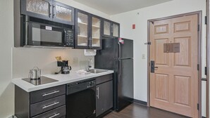 Eine kleine Küche mit Mikrowelle, Kühlschrank, Geschirrspüler und einer Holztür.