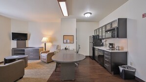 Ein modernes Hotelzimmer mit einem runden Esstisch, einer Couch, einem Fernseher, einer Lampe und einer Küchenzeile mit Mikrowelle und Kühlschrank.