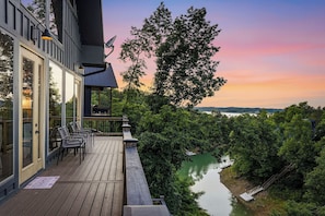 A wooden deck with chairs, a satellite dish, and a view of a river and forest.