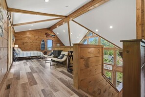 Un espacio tipo loft con paredes de madera y techo inclinado, que incluye un sofá, sillas y una mesita.