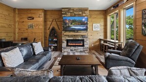 Ein gemütliches Blockhaus-Interieur mit Kamin aus Stein, Ledermöbeln und einem darüber hängenden Fernseher.