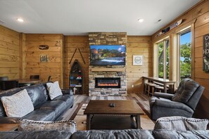L’intérieur chaleureux d’un chalet avec une cheminée en pierre, des meubles en cuir et un téléviseur fixé au-dessus.