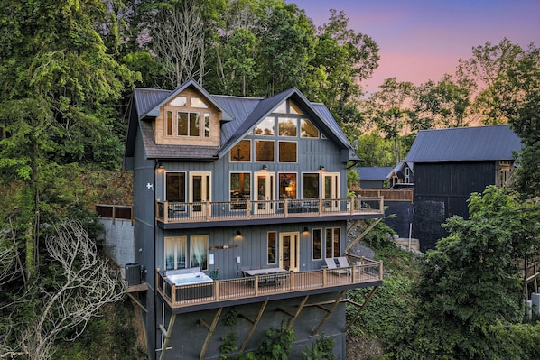 A multi-story house with a balcony, large windows, and a view of the surrounding forest.