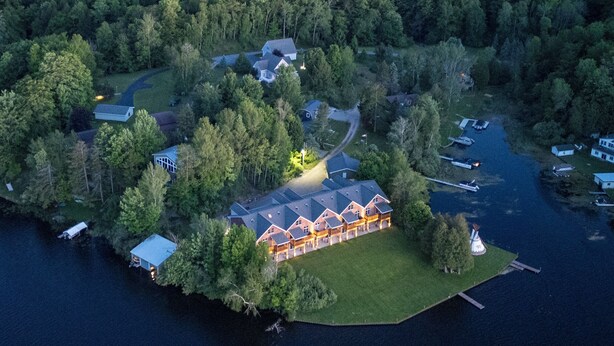 An aerial view of a lakeside property with a large house, a dock, and a boat.