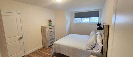 A bedroom with a bed, dresser, window, and ceiling light.