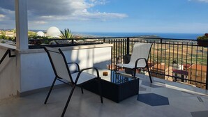 A balcony with two chairs and a glass-top table, overlooking a coastal landscape with buildings and a view of the sea. - B&B Monte (Giardina Gallotti)