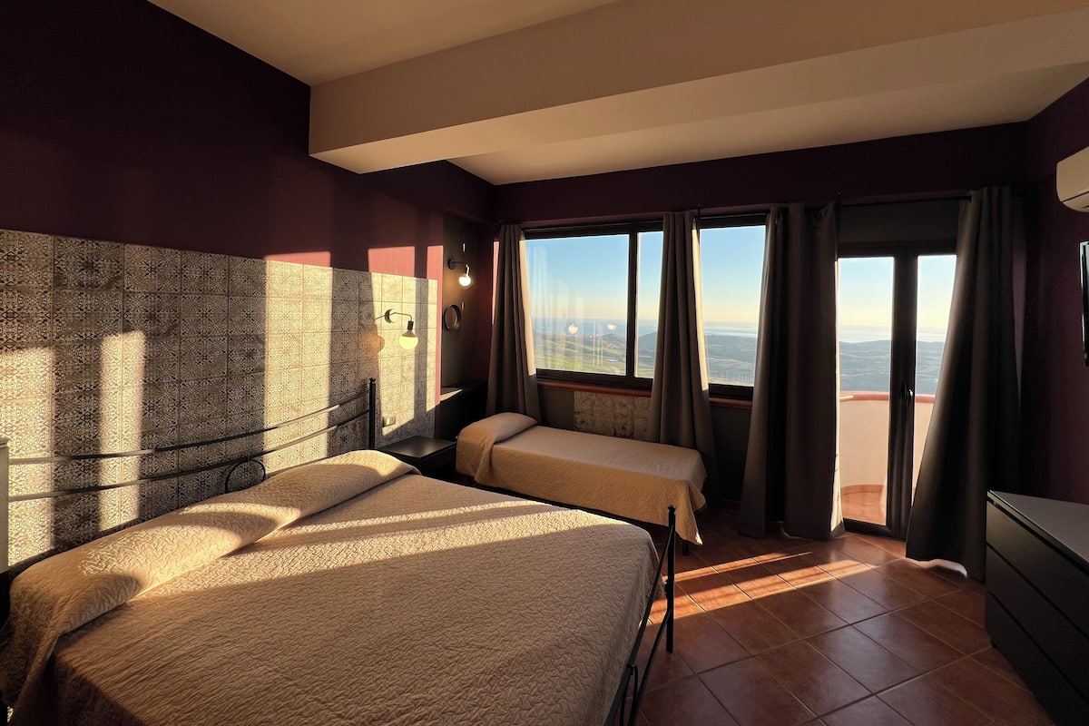 A hotel room with two beds, a view of the cityscape, and a balcony with curtains.
