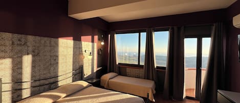 Habitación de hotel con dos camas, vista a la ciudad y un balcón con cortinas.