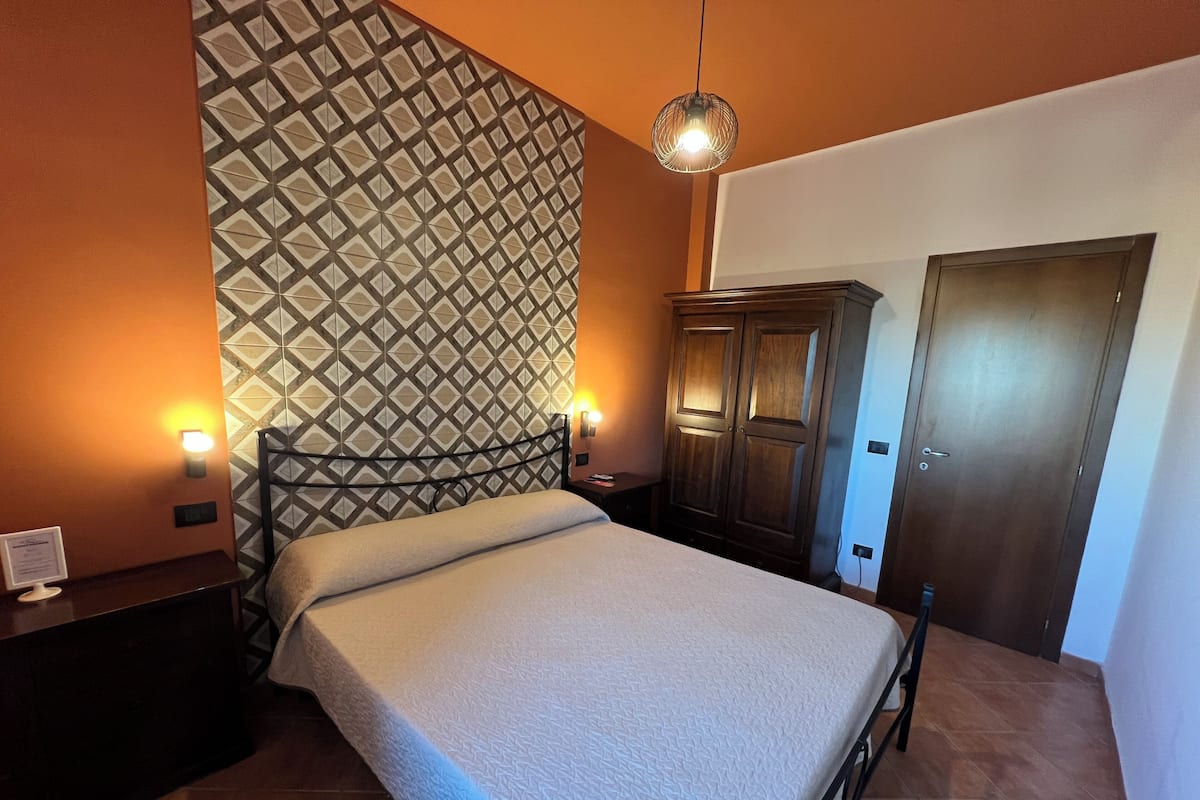 A bedroom with a bed, two bedside tables, a wardrobe, and a patterned wall.