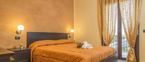 Une chambre avec un grand lit, deux tables de chevet avec des lampes, une fenêtre avec des rideaux et une vue sur l’extérieur.