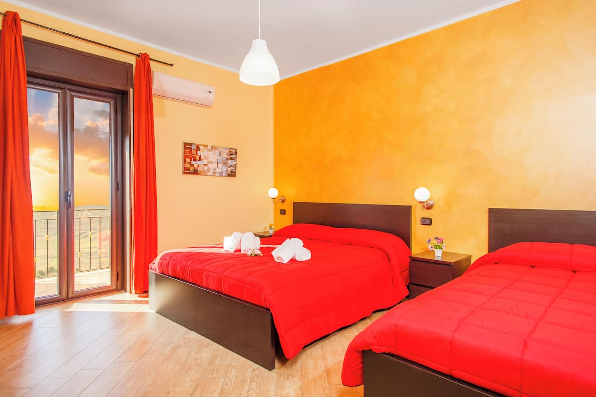 A hotel room with two beds, a balcony, a painting, and a nightstand with a lamp.