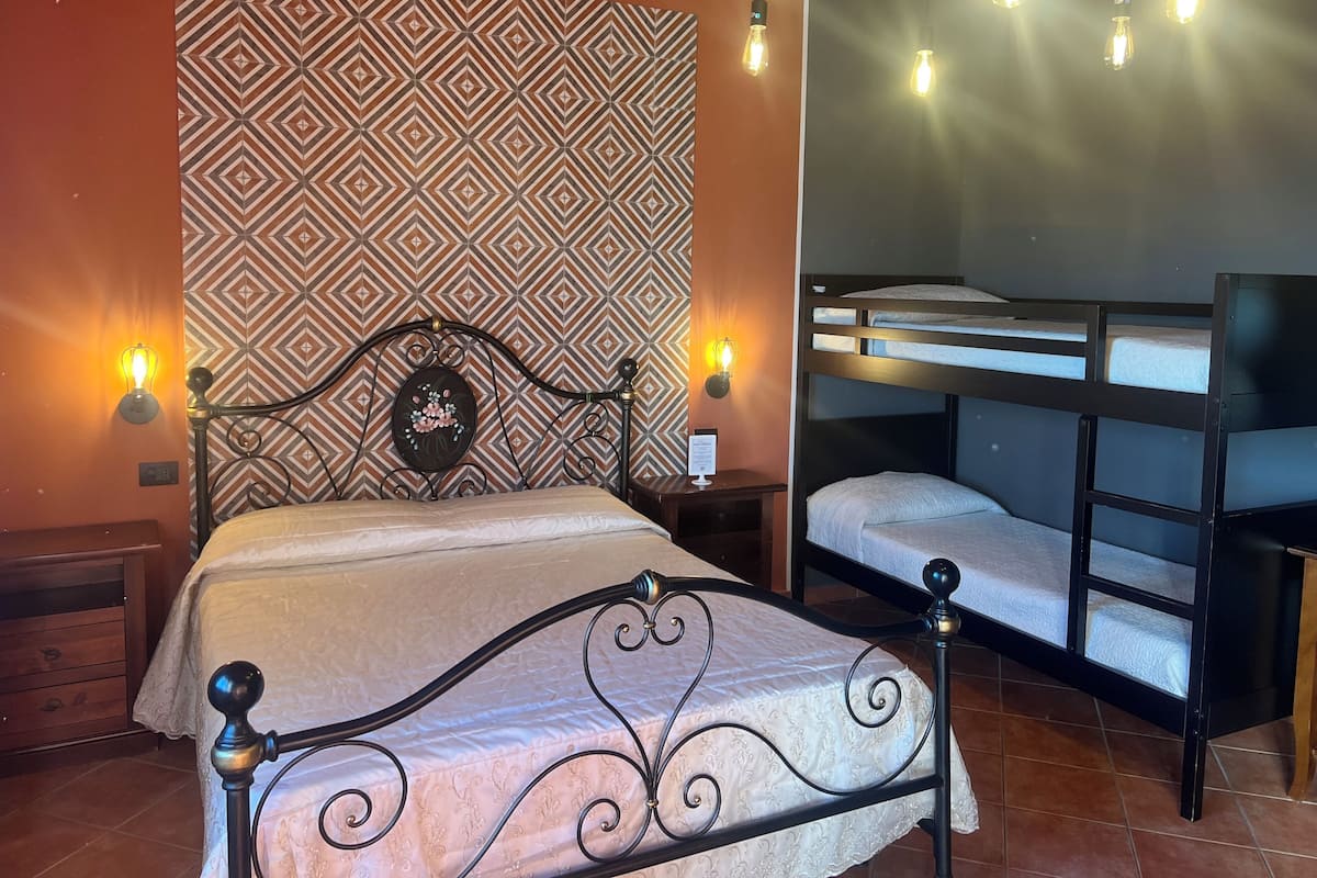 A bedroom with a patterned wallpaper, a bed with a decorative headboard, a nightstand, and a bunk bed.
