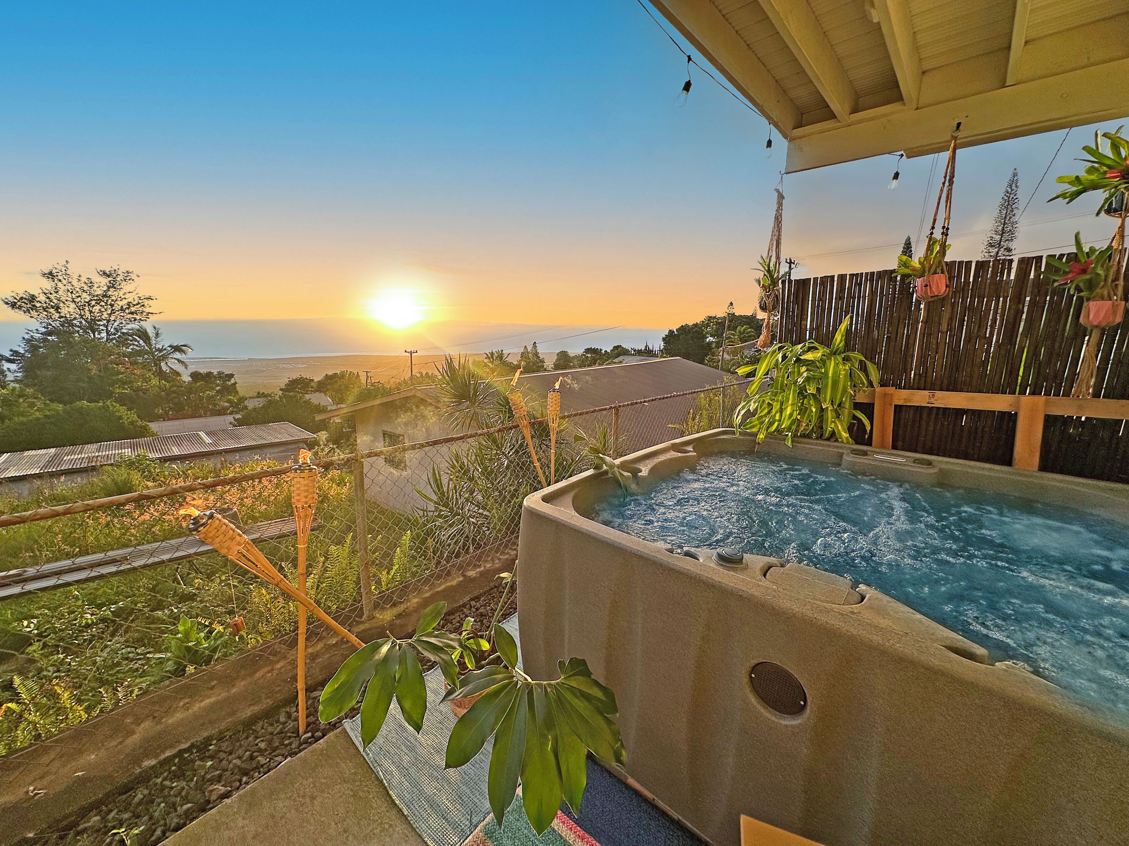 Un bain à remous avec vue sur le coucher de soleil, entouré de verdure et délimité par une clôture en bois.