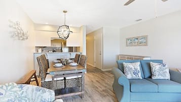 A modern living room with a blue sofa, a dining table with chairs, and a ceiling fan.