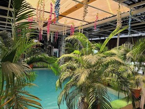 Zona de piscina interior con palmeras y decoración floral colgante.