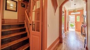 Un escalier en bois menant à une porte dotée de panneaux de verre, un couloir avec un plancher en bois et une porte en arc de cercle.