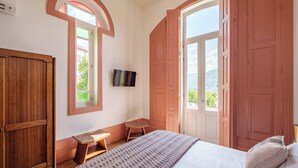 Une chambre à coucher comprenant un lit, un bureau, une chaise, un téléviseur et de grandes fenêtres avec des portes.