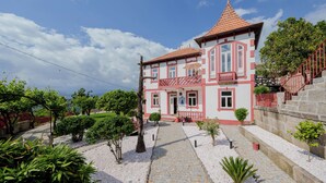 Un bâtiment à deux étages, doté d’un toit recouvert de tuiles rouges, d’un balcon et d’un escalier en pierre menant à l’entrée.