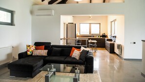 A modern living room with a black sectional sofa, a glass coffee table, and a kitchen in the background. - MAISON DE VACANCES près de Thermes de Bucarest & Otopeni Airport (Balotesti)