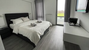 A modern hotel room with a large bed, a bedside table with a coffee maker, a view of a green field through the window, and a sliding door to the balcony. - MAISON DE VACANCES près de Thermes de Bucarest & Otopeni Airport (Balotesti)