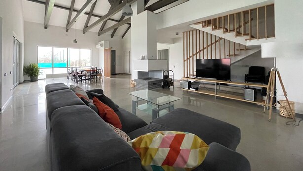 A spacious living area with a modern design, featuring a large sofa, a glass coffee table, and a flat-screen TV. A staircase with wooden railings leads to an upper level. - MAISON DE VACANCES près de Thermes de Bucarest & Otopeni Airport (Balotesti)