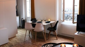 Un comedor con una mesa para dos, un cubo de basura y una ventana con vistas a edificios.