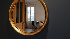 Espejo redondo con marco dorado que refleja una habitación con una mesa de comedor, sillas y una ventana.