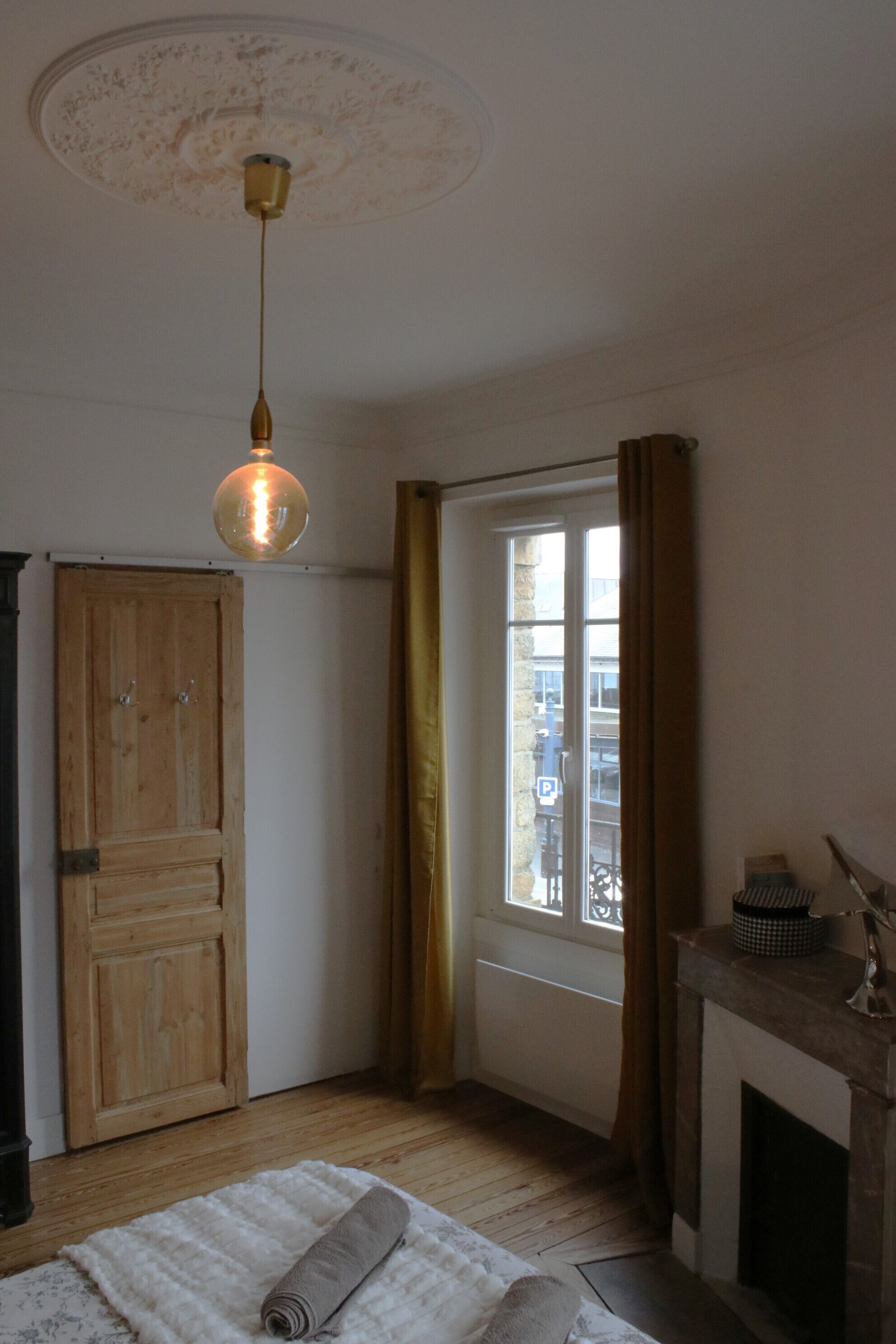 A room with a wooden door, a window with curtains, a fireplace, and a hanging light fixture.