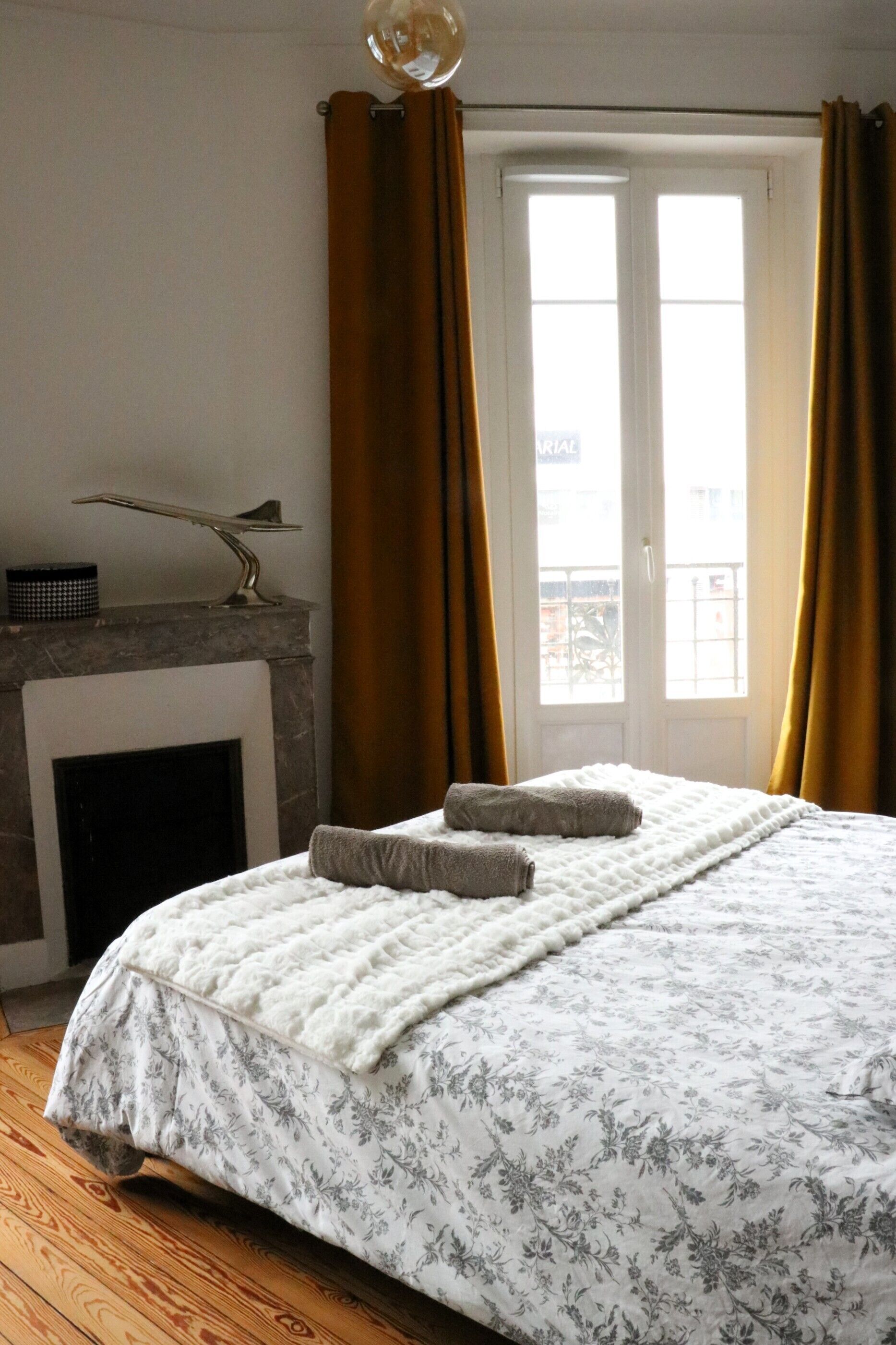 Un dormitorio con cama, chimenea y vistas a través de una ventana con cortinas.