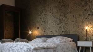 Un dormitorio con cama, almohadas, mesita de noche, lámpara y pared con diseño.