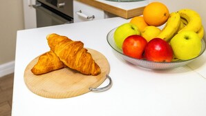 Eine Küche mit weißer Arbeitsplatte, einer Glaskaffeekanne und einer Schüssel mit Obst und Croissants.