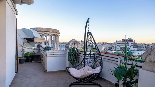 Ein Hängekorbstuhl auf einem Balkon mit Topfpflanzen und Blick auf die Stadt.
