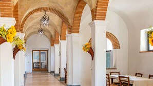 A corridor with arched brick ceilings, white walls, and hanging chandeliers. There are wicker baskets with flowers on either side of the corridor. - Agr. Lampugnano (Civitella Paganico)
