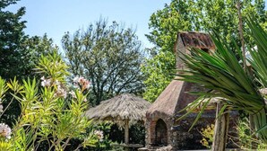 A rustic stone structure with a thatched roof, surrounded by lush greenery and flowering plants. - Agr. Lampugnano (Civitella Paganico)